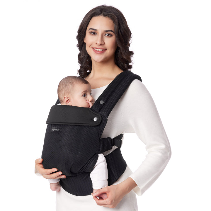 Mother in white top holding baby in black Momcozy ergonomic carrier for comfort.