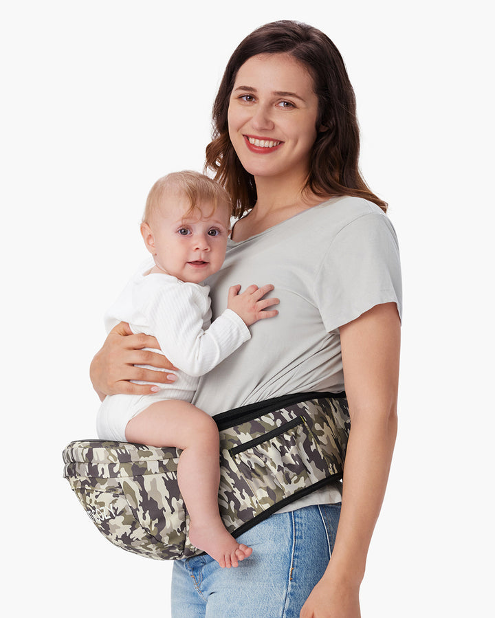 Woman holding baby using Momcozy baby hip seat carrier with a camouflage design; both are smiling, baby dressed in white onesie; ideal for comfortable and secure baby carrying.