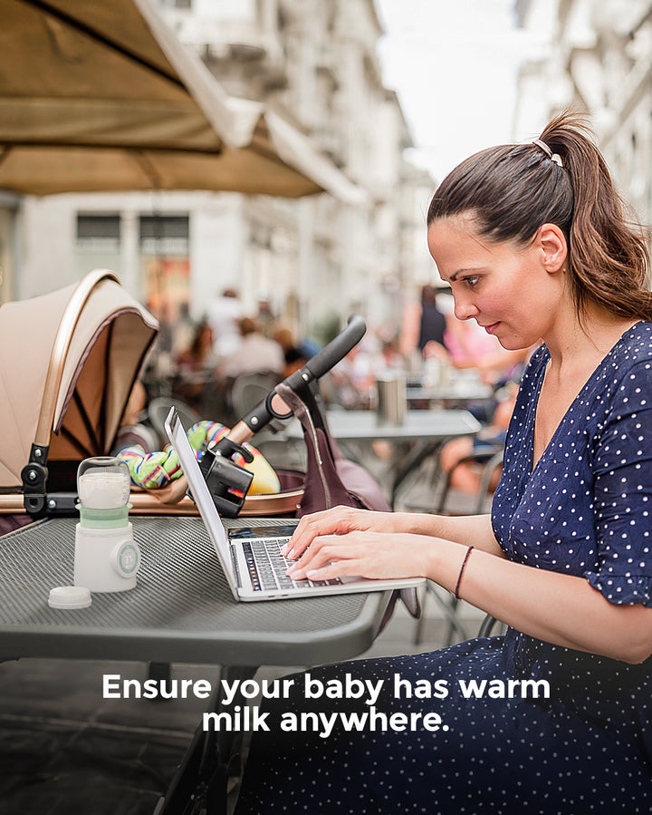 Mom using laptop in a café with portable baby bottle warmer for travel.