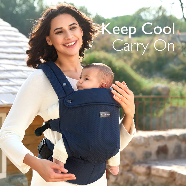 Mother comfortably carrying baby in navy Momcozy ergonomic carrier with breathable fabric.