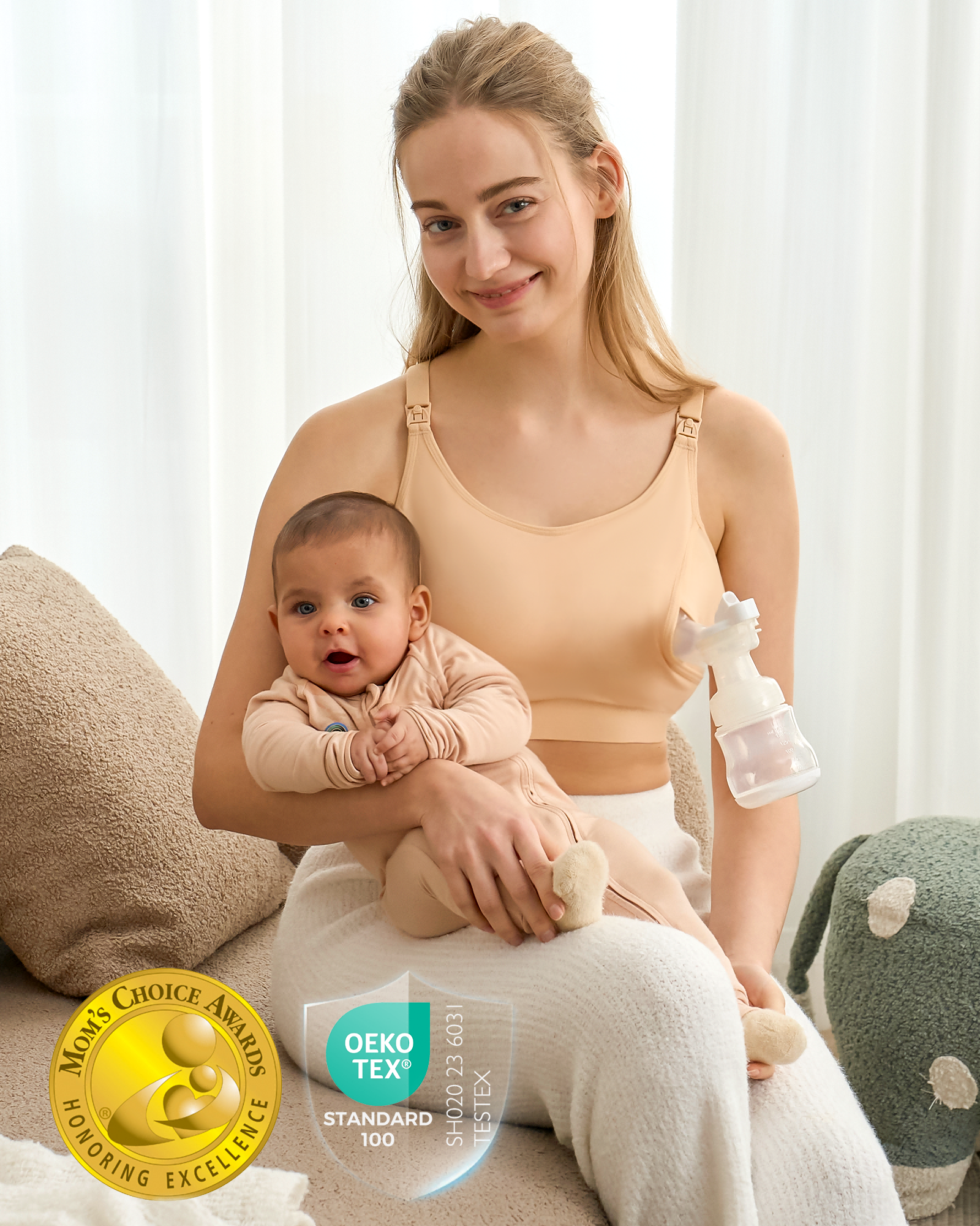 Smiling blonde mom in beige YN08 pumping bra, hands-free while holding her baby. Features Mom's Choice & OEKO-TEX for safety.