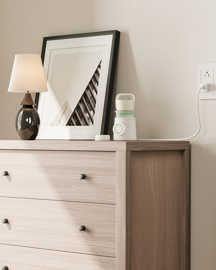 Cordless portable baby bottle warmer with a large-capacity battery, currently charging on a dresser.