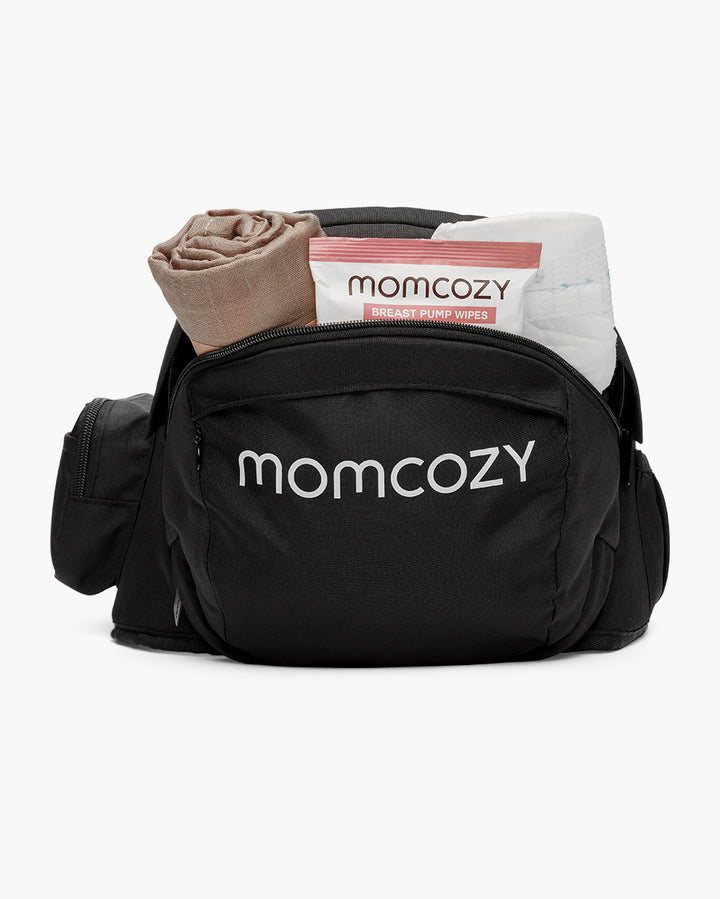 Black Momcozy bag showing front pocket with visible brand logo, containing a rolled-up cloth and a packet of Momcozy breast pump wipes.