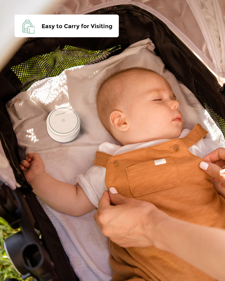 Momcozy Portable Baby Sound Machine beside sleeping baby in stroller, highlighting portability.