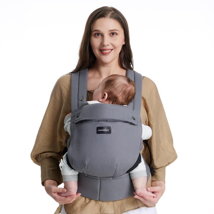 Mom holding baby in gray Momcozy baby carrier designed for comfort and support. Essential for travel and everyday use, as part of baby carrier bundle including a baby bottle warmer.